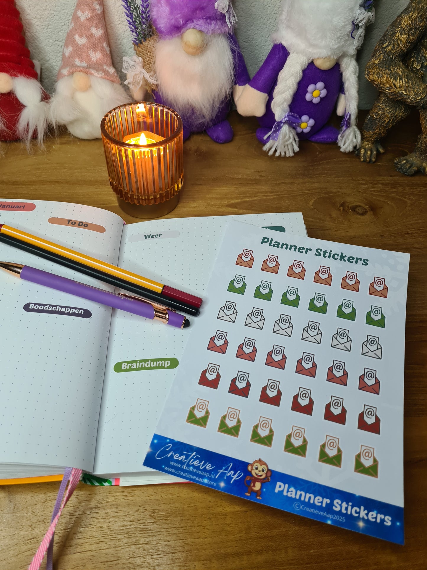 Handgemaakte planner stickers met email icoon in diverse kleuren, beschikbaar in A6 en A5, met keuze uit matte of glanzende afwerking. Ideaal voor het plannen en organiseren van e-mails en digitale taken in planners of bullet journals. Te zien in een warme en gezellige setting met kaarslicht en creatieve accessoires.