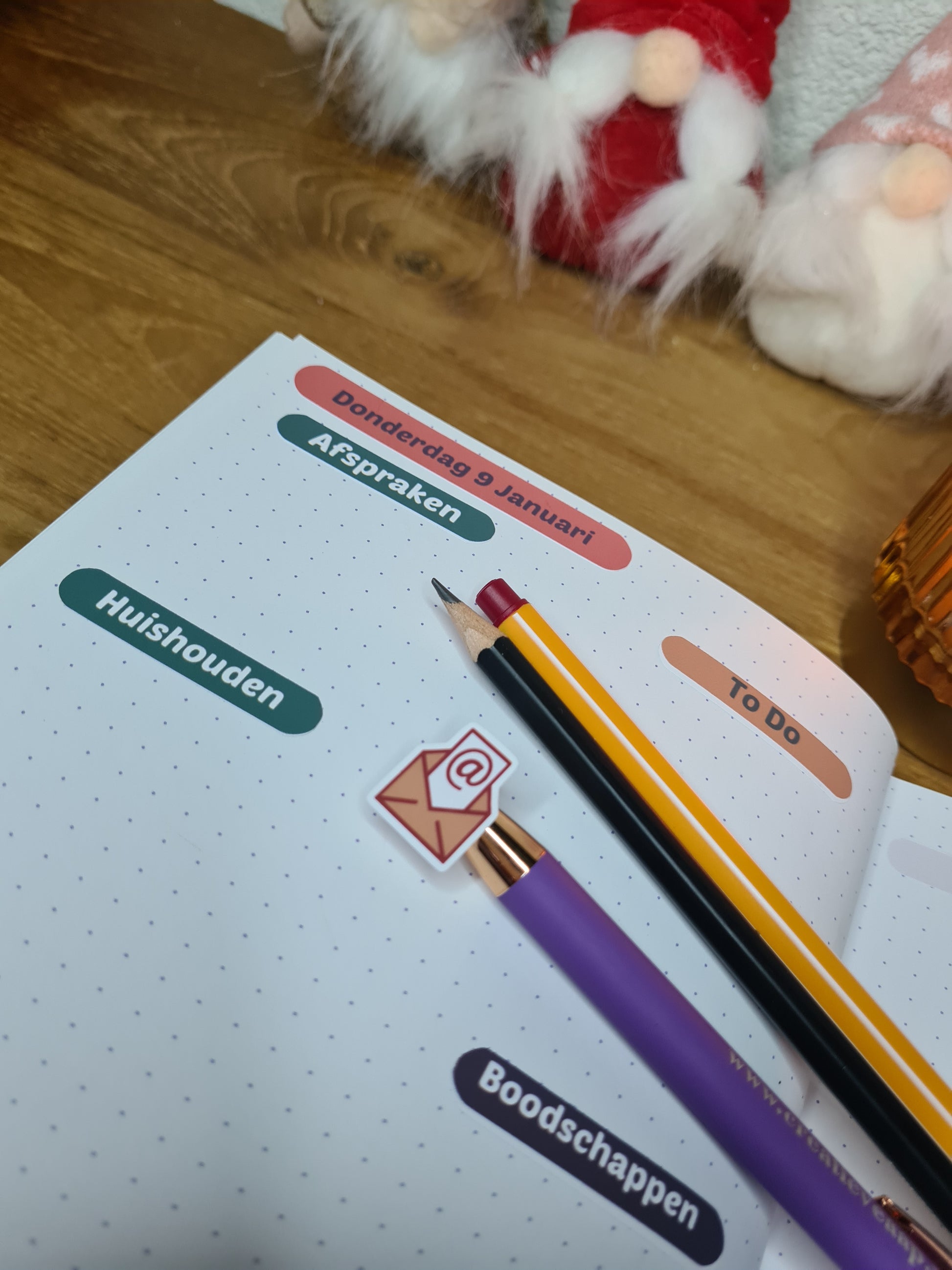 Handgemaakte planner stickers met email icoon in diverse kleuren, beschikbaar in A6 en A5, met keuze uit matte of glanzende afwerking. Ideaal voor het plannen en organiseren van e-mails en digitale taken in planners of bullet journals. Te zien in een warme en gezellige setting met kaarslicht en creatieve accessoires.