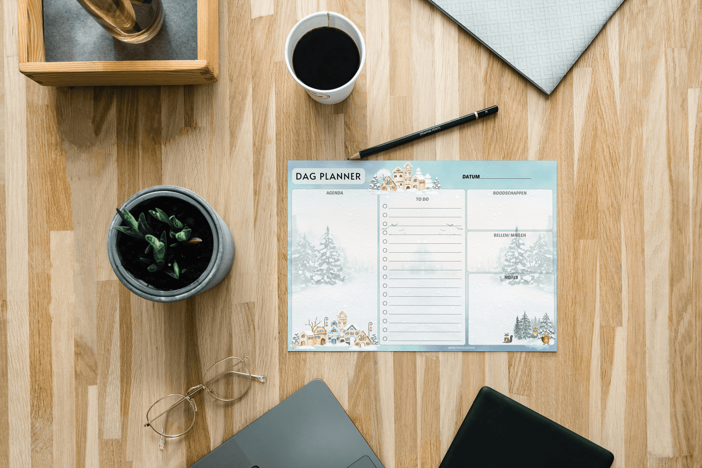 Dagplanner Winter 2025 – Handgemaakt notitieblok met winters thema, liggend op een houten bureau met koffie, plant en laptop. Perfect voor dagelijkse planning.