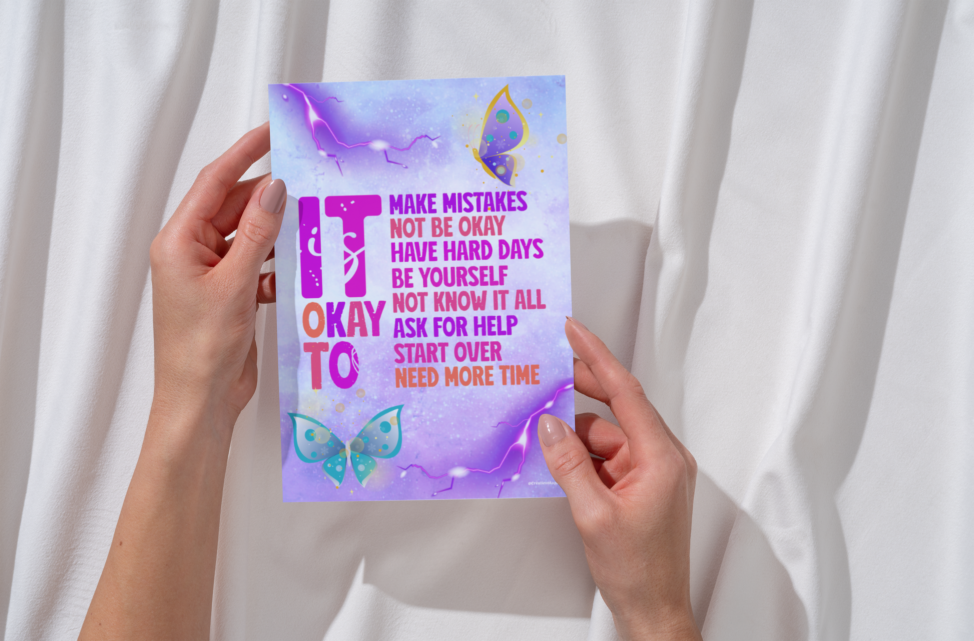 Motiverende Print Art 'It's Okay To' met een kleurrijk ontwerp in paarse en blauwe tinten, versierd met vlinders en een inspirerende boodschap, weergegeven in verschillende stijlen zoals ingelijst, op een tafel en in handen, beschikbaar in A6 en A5 formaat.